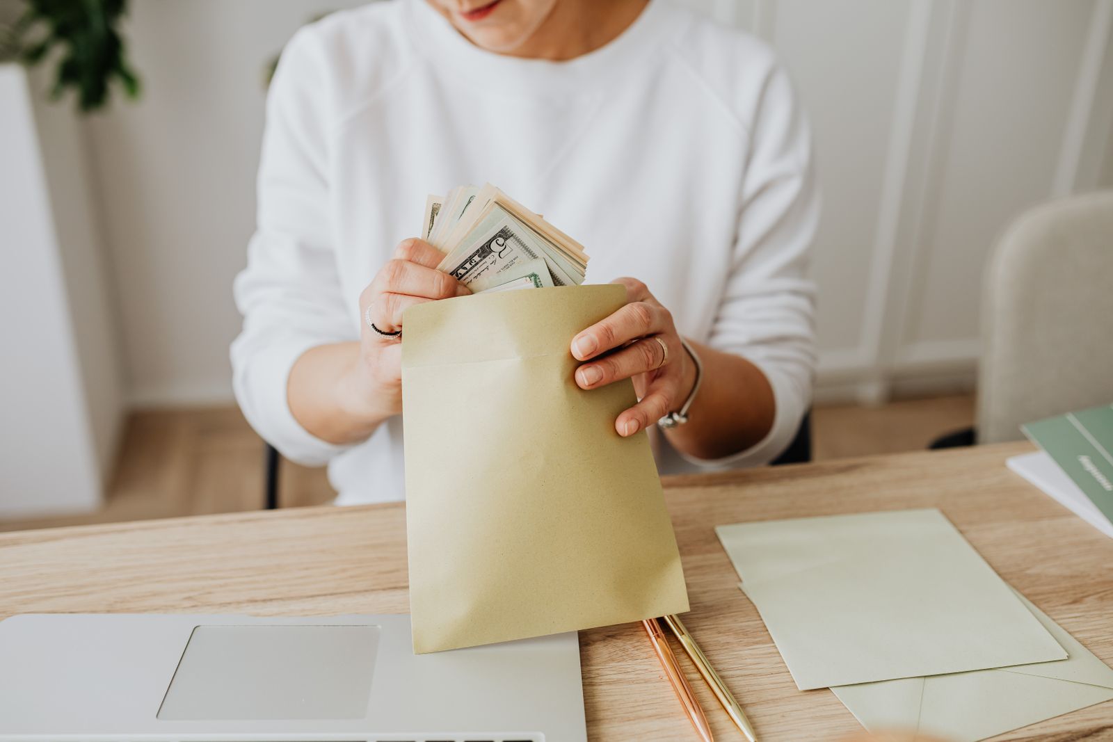 A person at a desk placing banknotes into a kraft-paper envelope.